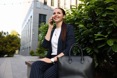 Photo of Successful businesswoman talking on phone near office building