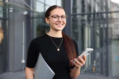 Photo of Successful businesswoman with smartphone and folder near office building