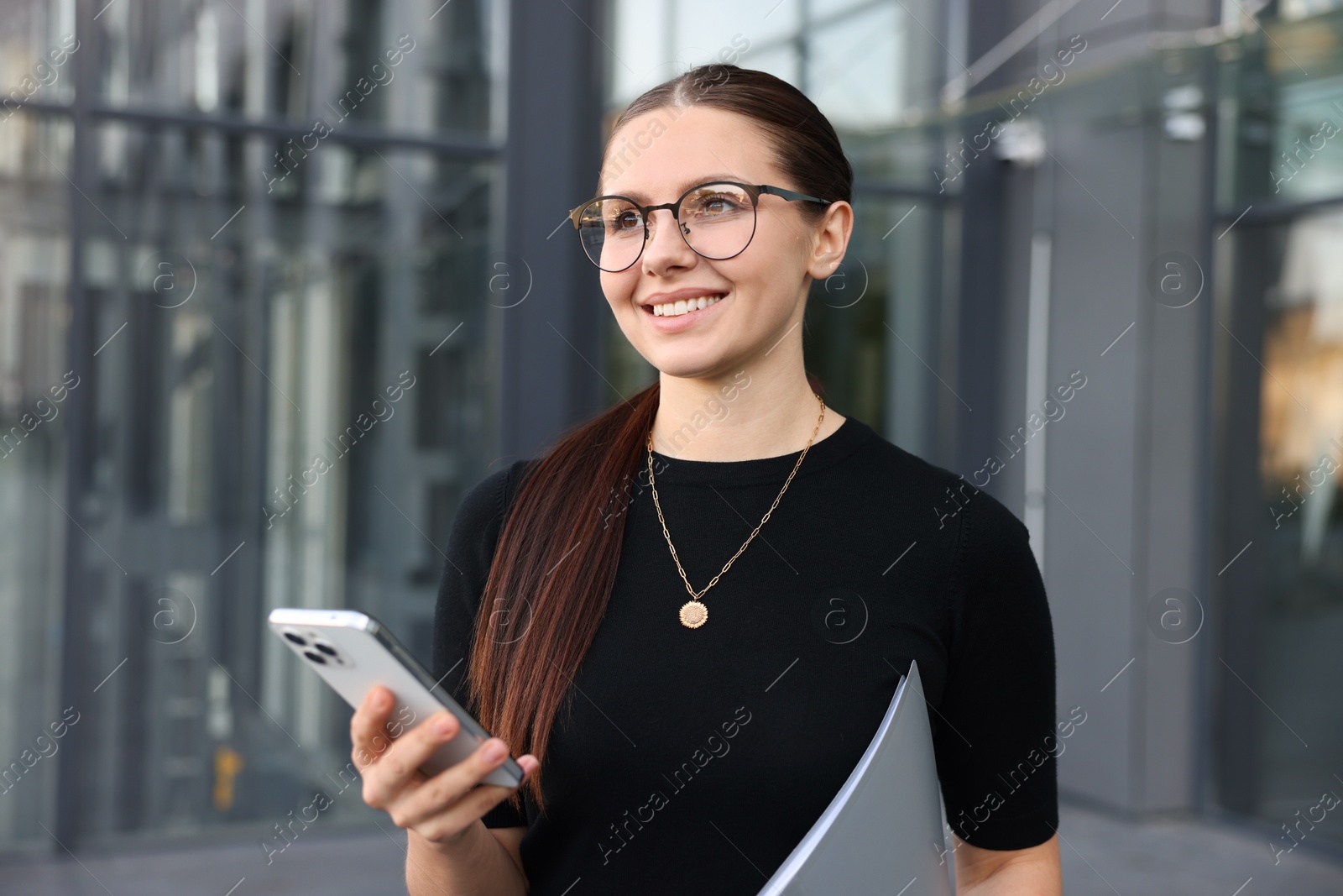 Successful businesswoman with smartphone and folder near office building Photo of Successful businesswoman with smartphone and folder near office building