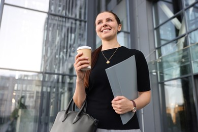 Photo of Successful businesswoman with coffee and folder near office building, low angle view