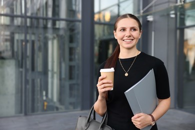 Photo of Successful businesswoman with coffee and folder near office building. Space for text