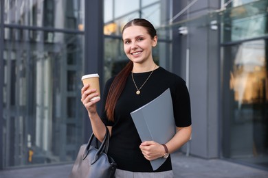 Photo of Successful businesswoman with coffee and folder near office building