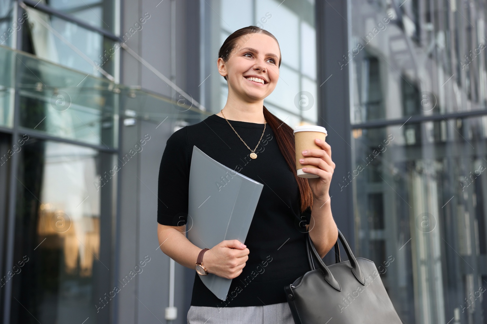 Successful businesswoman with coffee and folder near office building Photo of Successful businesswoman with coffee and folder near office building