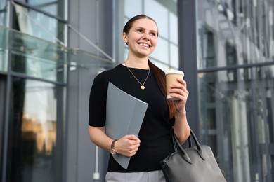 Photo of Successful businesswoman with coffee and folder near office building
