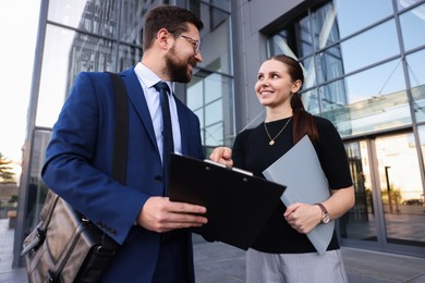 Photo of Happy coworkers discussing something near office building, low angle view