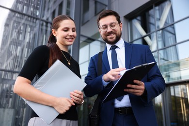 Photo of Happy coworkers discussing something near office building, low angle view
