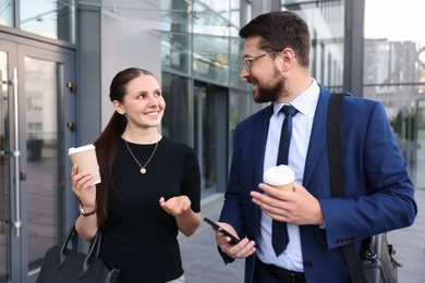 Photo of Happy coworkers with coffee discussing something near office building