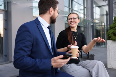 Photo of Happy coworkers with smartphone and coffee discussing something near office building