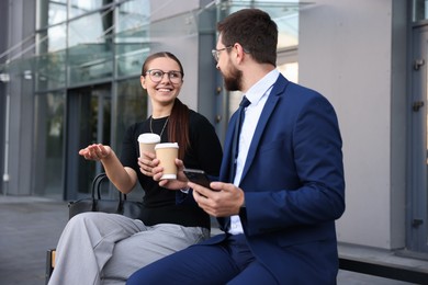 Photo of Happy coworkers with smartphone and coffee discussing something near office building