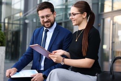 Photo of Happy coworkers with tablet discussing something near office building