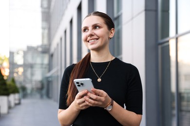 Photo of Successful businesswoman with smartphone near office building