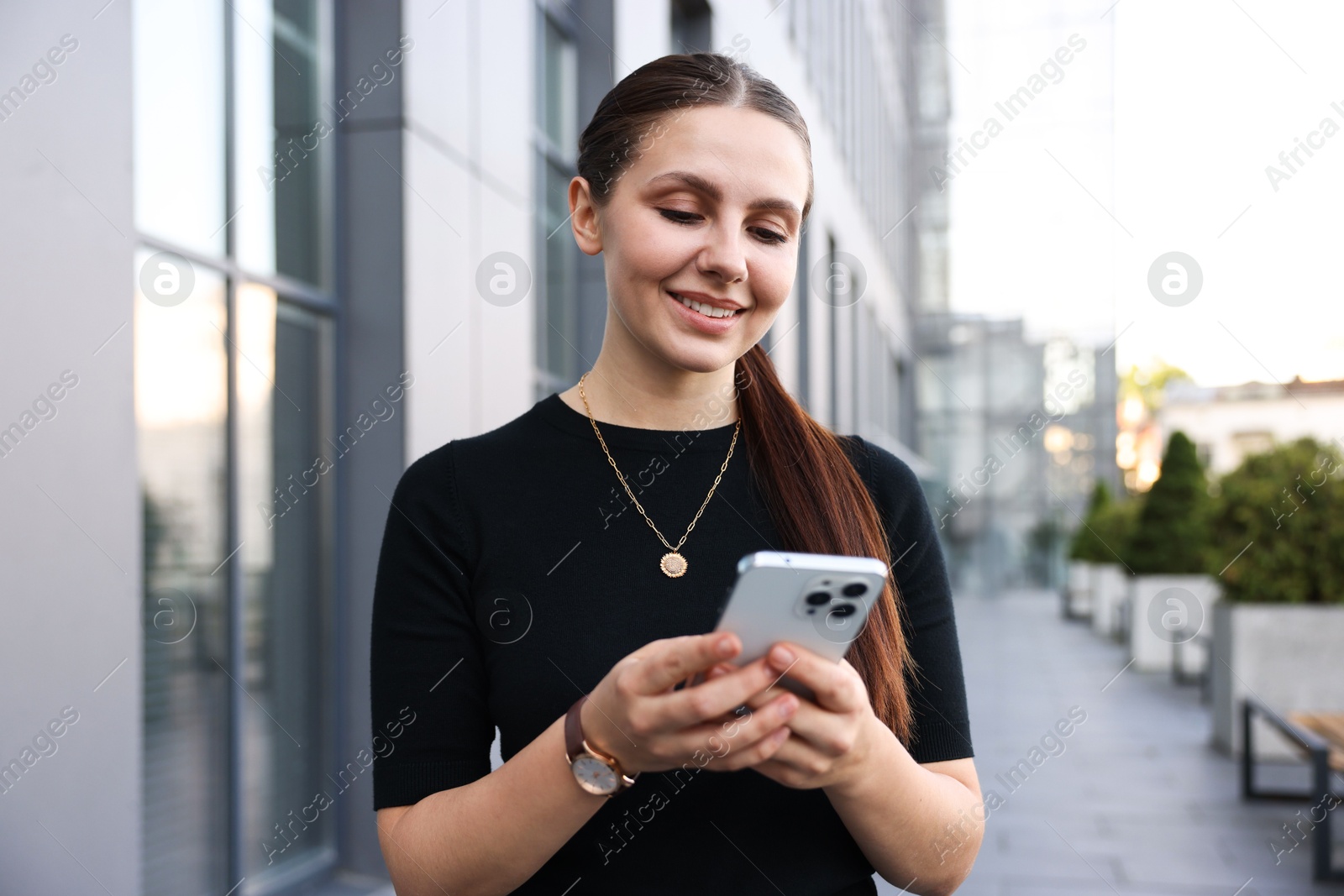 Photo of Successful businesswoman with smartphone near office building