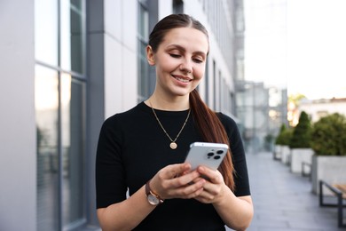 Photo of Successful businesswoman with smartphone near office building