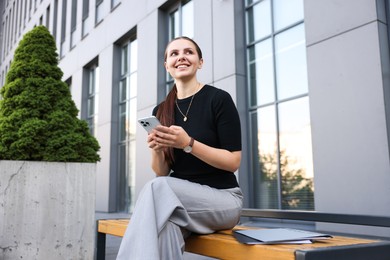 Photo of Successful businesswoman with smartphone near office building