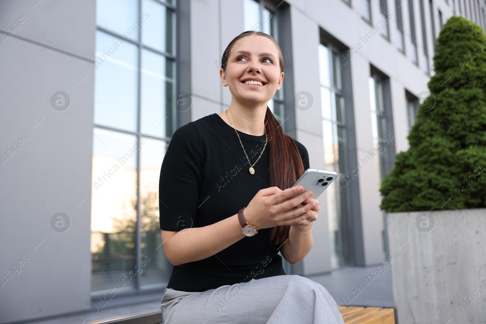 Photo of Successful businesswoman with smartphone near office building