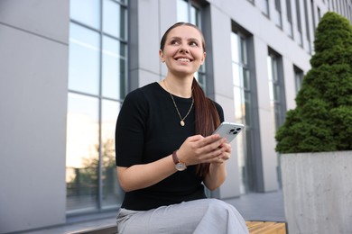 Photo of Successful businesswoman with smartphone near office building