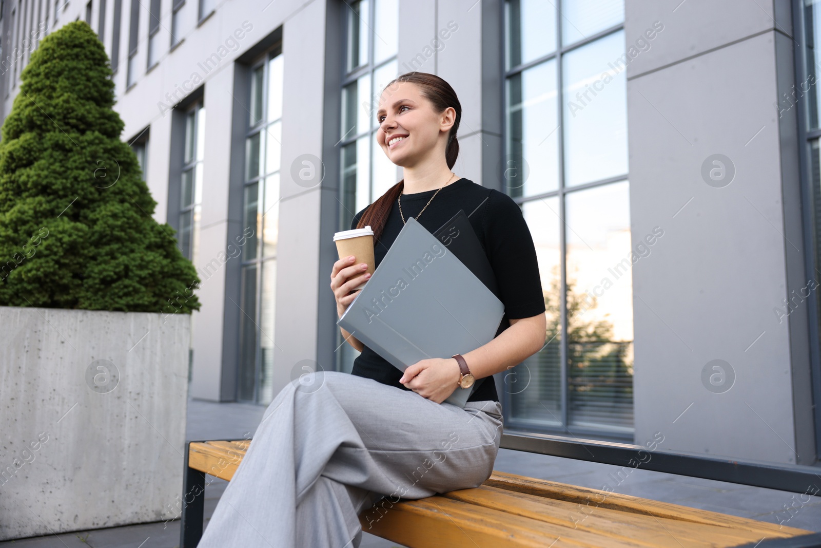 Successful businesswoman with coffee and folder near office building Photo of Successful businesswoman with coffee and folder near office building