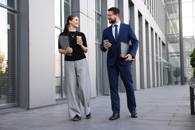 Photo of Happy coworkers with smartphone and coffee discussing something near office building
