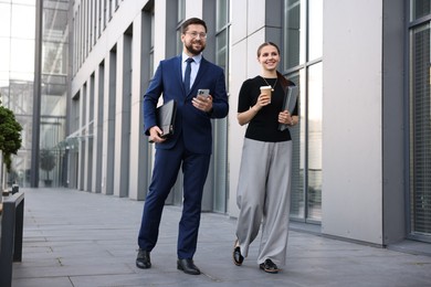 Photo of Happy coworkers with smartphone and coffee discussing something near office building