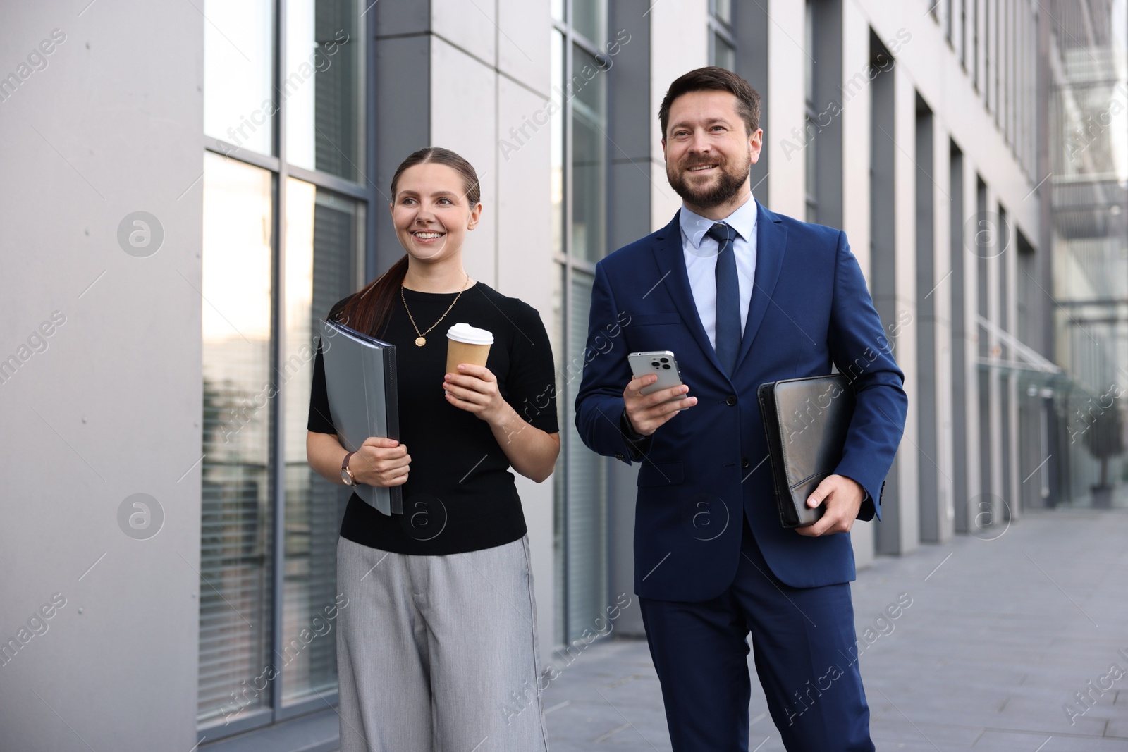 Photo of Happy coworkers with smartphone and coffee discussing something near office building