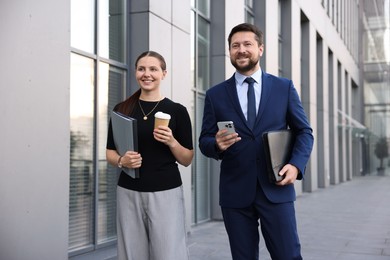 Photo of Happy coworkers with smartphone and coffee discussing something near office building