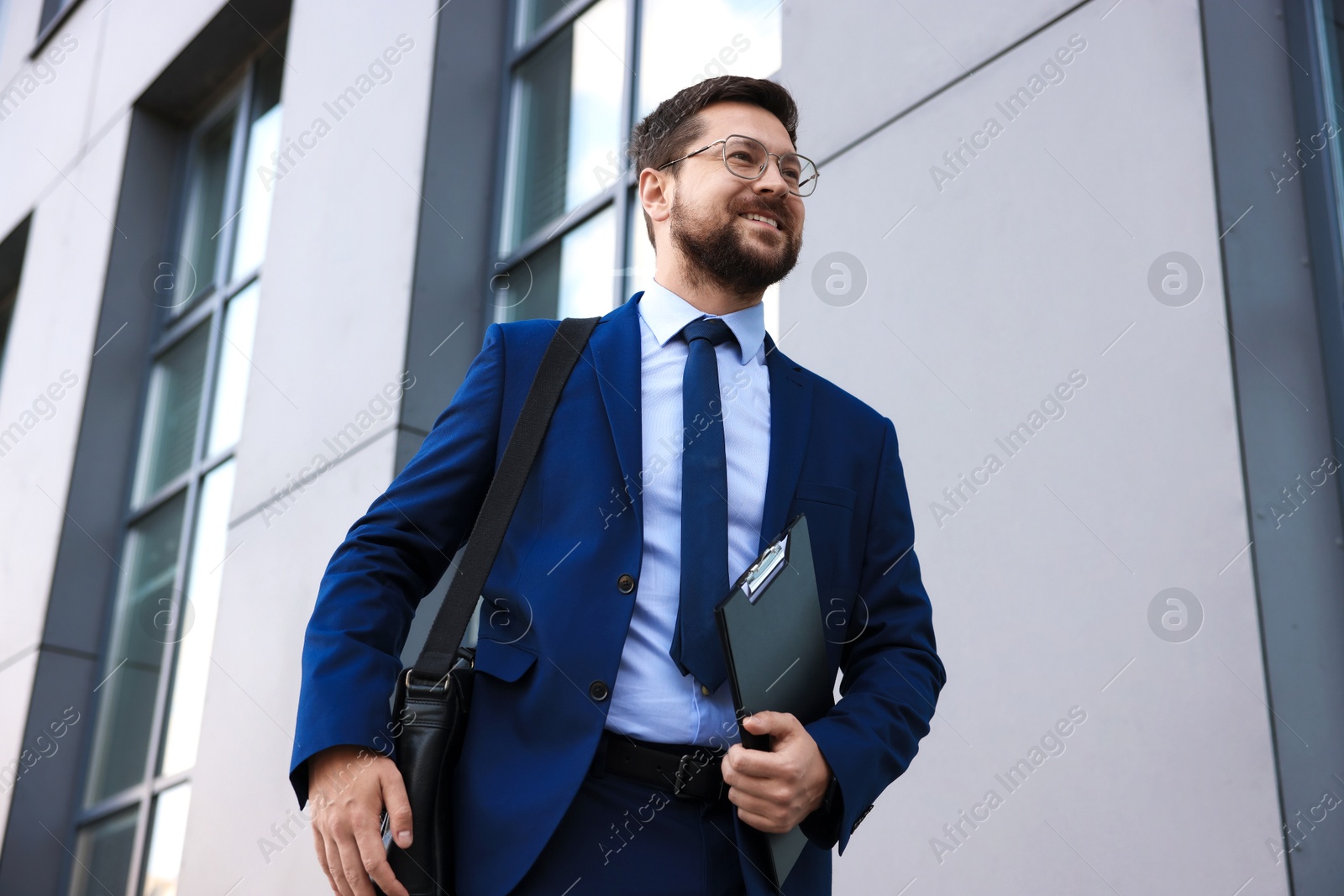 Photo of Successful businessman with clipboard near office building, low angle view