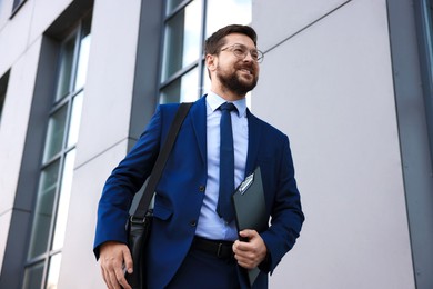 Photo of Successful businessman with clipboard near office building, low angle view