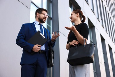 Photo of Happy coworkers discussing something near office building, low angle view