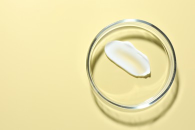 Photo of Cosmetic product in Petri dish on pale yellow background, top view. Space for text