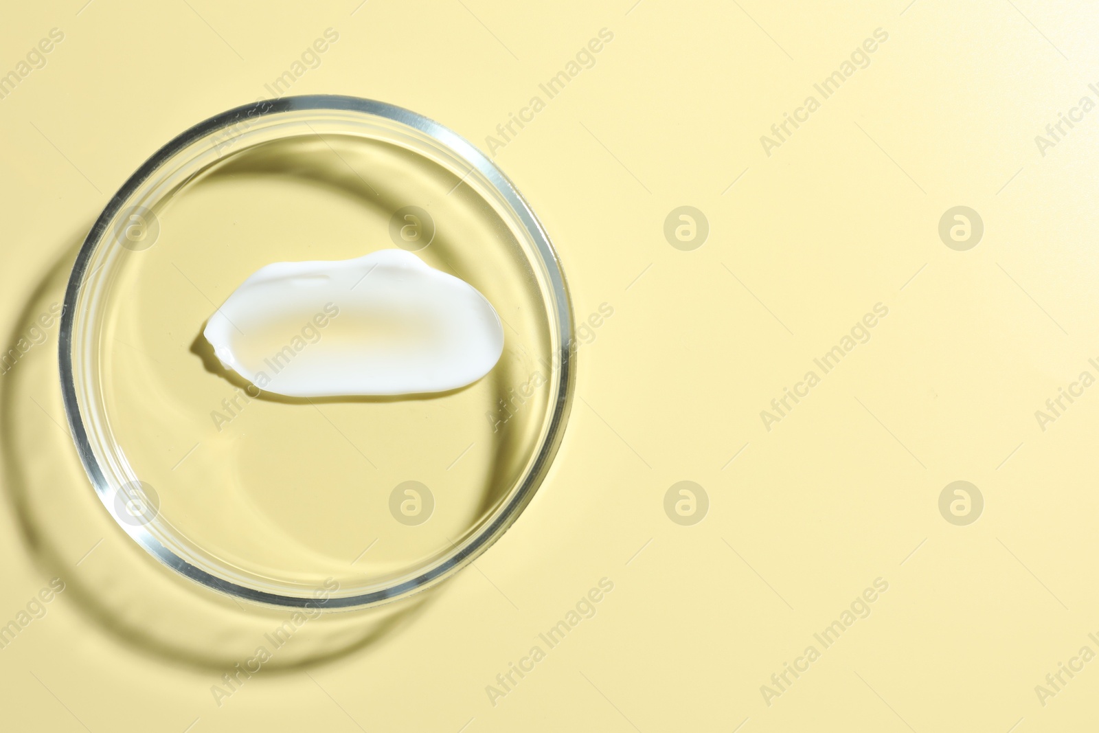 Cosmetic product in Petri dish on pale yellow background, top view. Space for text Photo of Cosmetic product in Petri dish on pale yellow background, top view. Space for text