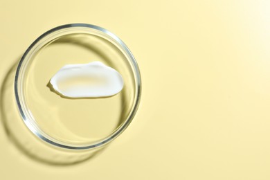 Photo of Cosmetic product in Petri dish on pale yellow background, top view. Space for text
