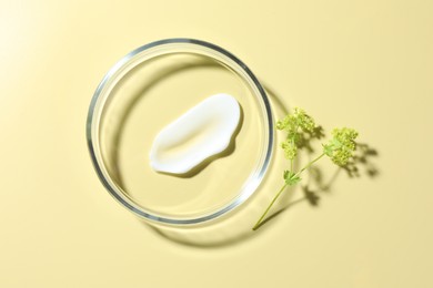 Photo of Cosmetic product in Petri dish and floral decor on pale yellow background, flat lay