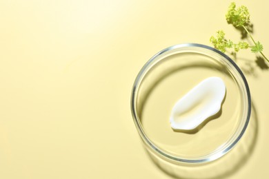 Photo of Cosmetic product in Petri dish and floral decor on pale yellow background, flat lay. Space for text