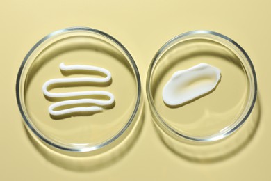 Photo of Different cosmetic products in Petri dishes on pale yellow background, flat lay