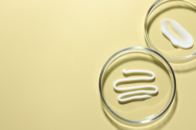 Photo of Different cosmetic products in Petri dishes on pale yellow background, flat lay. Space for text