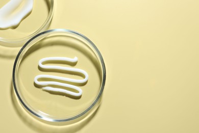 Photo of Different cosmetic products in Petri dishes on pale yellow background, flat lay. Space for text