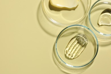 Photo of Different cosmetic products in Petri dishes on pale yellow background, flat lay. Space for text
