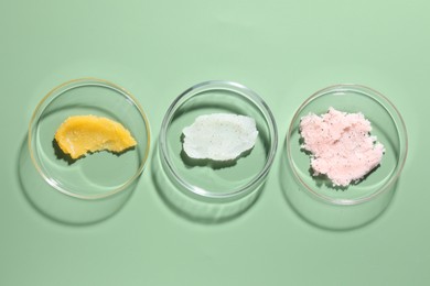 Photo of Different cosmetic products in Petri dishes on green background, flat lay