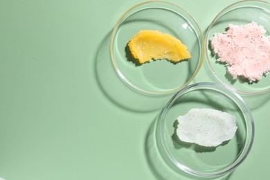 Photo of Different cosmetic products in Petri dishes on green background, flat lay. Space for text