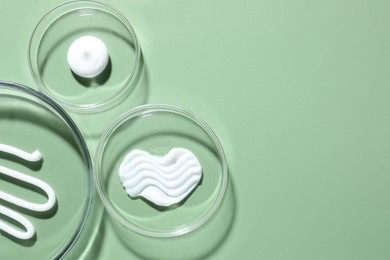 Photo of Different cosmetic products in Petri dishes on green background, flat lay. Space for text