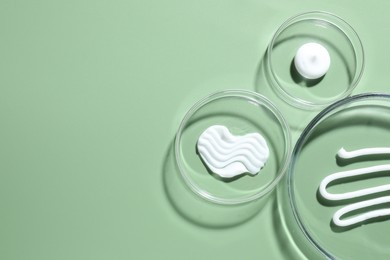 Photo of Different cosmetic products in Petri dishes on green background, flat lay. Space for text