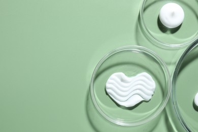 Photo of Different cosmetic products in Petri dishes on green background, flat lay. Space for text