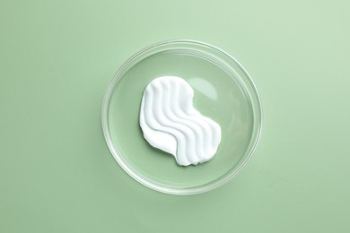 Photo of Cosmetic product in Petri dish on green background, top view