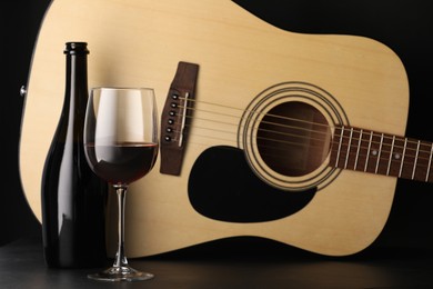 Photo of Acoustic guitar and red wine on black table, closeup