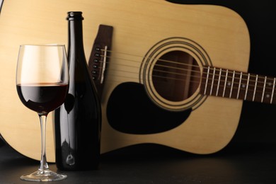 Photo of Acoustic guitar and red wine on black table, closeup