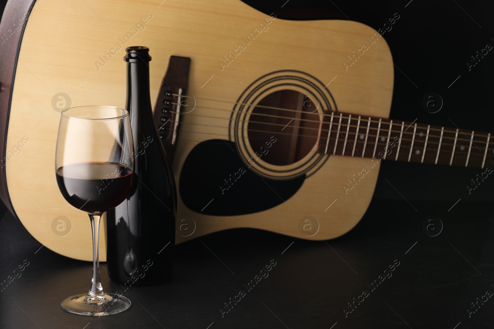 Photo of Acoustic guitar and red wine on black table, closeup