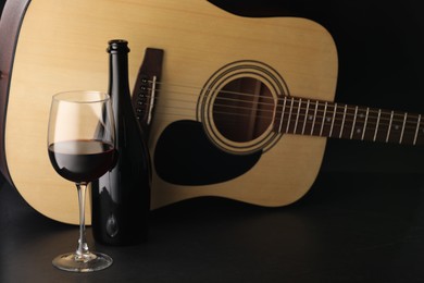 Photo of Acoustic guitar and red wine on black table, closeup
