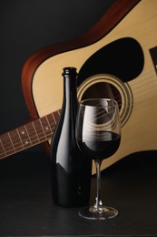 Photo of Acoustic guitar and red wine on black table, closeup