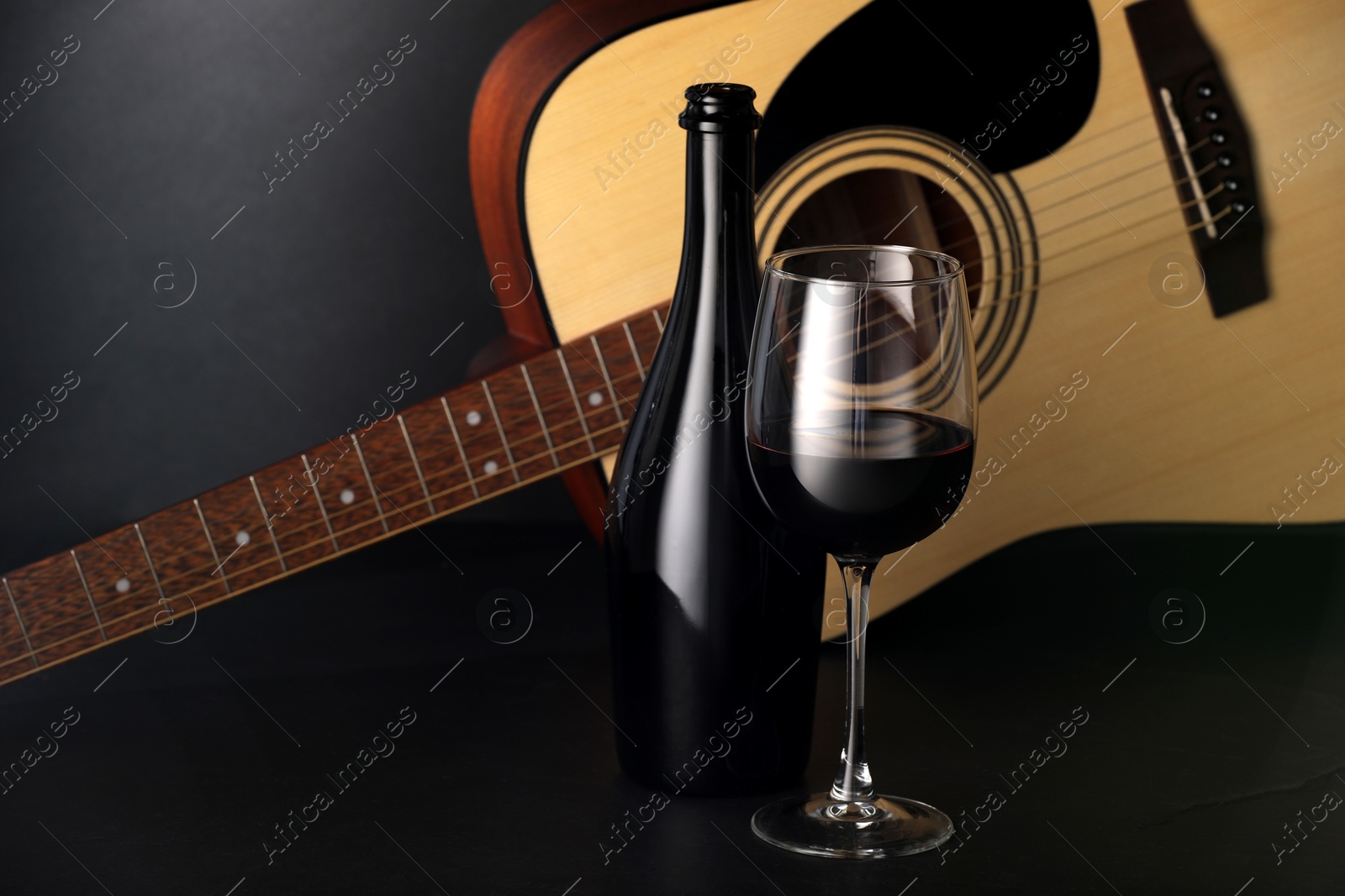 Photo of Acoustic guitar and red wine on black table, closeup