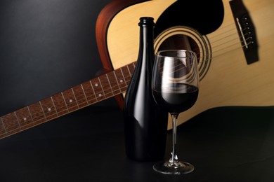 Photo of Acoustic guitar and red wine on black table, closeup